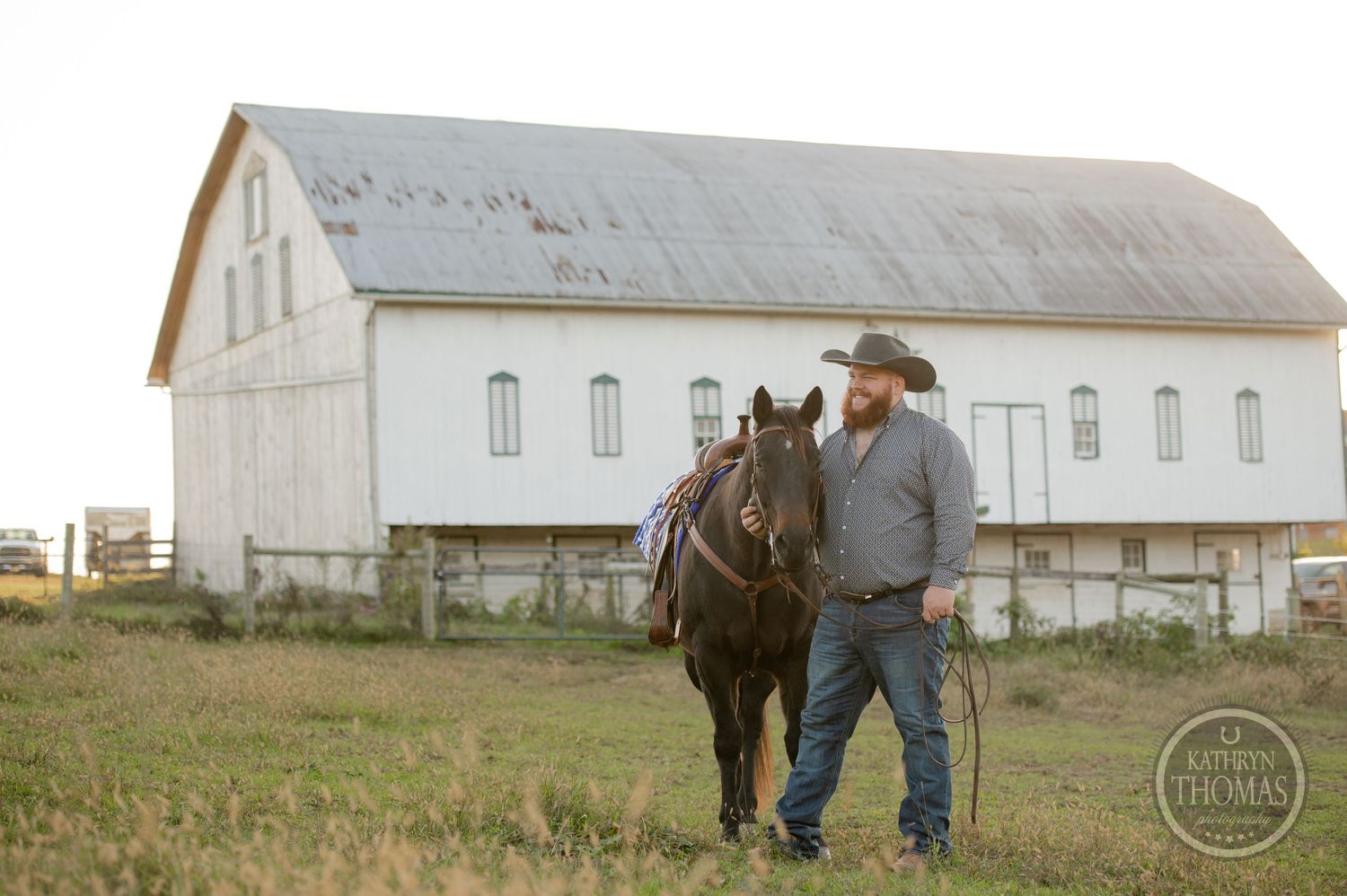 Horse and handler stand together near large white barn structure.