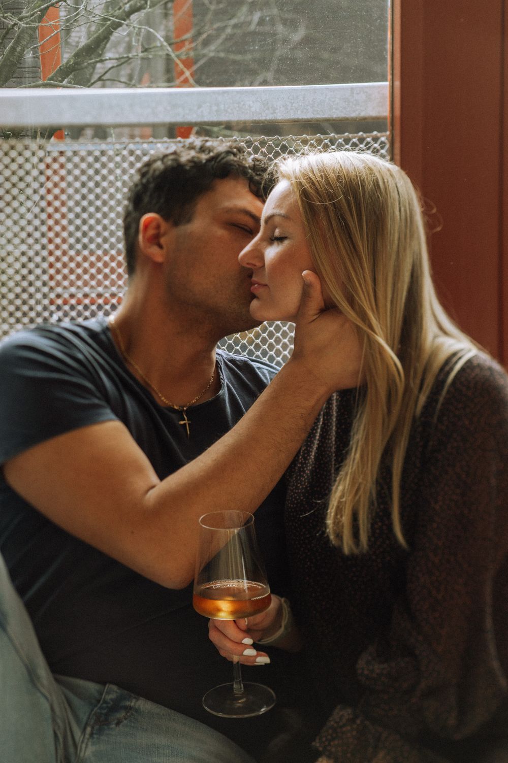 A romantic couple shares drinks and kisses in a cozy indoor setting.