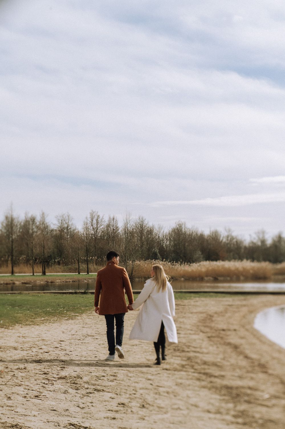 A couple takes a romantic walk along a sandy beach on a cloudy winter day.