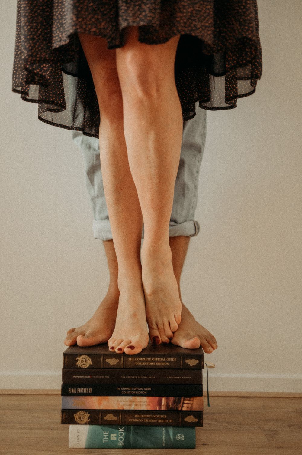 Bare feet standing on stacked vintage books against a neutral background.