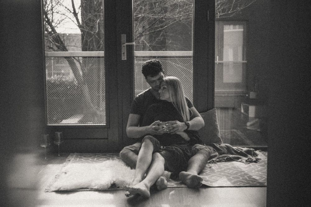 Couple relaxing together by large windows in moody black and white photography.