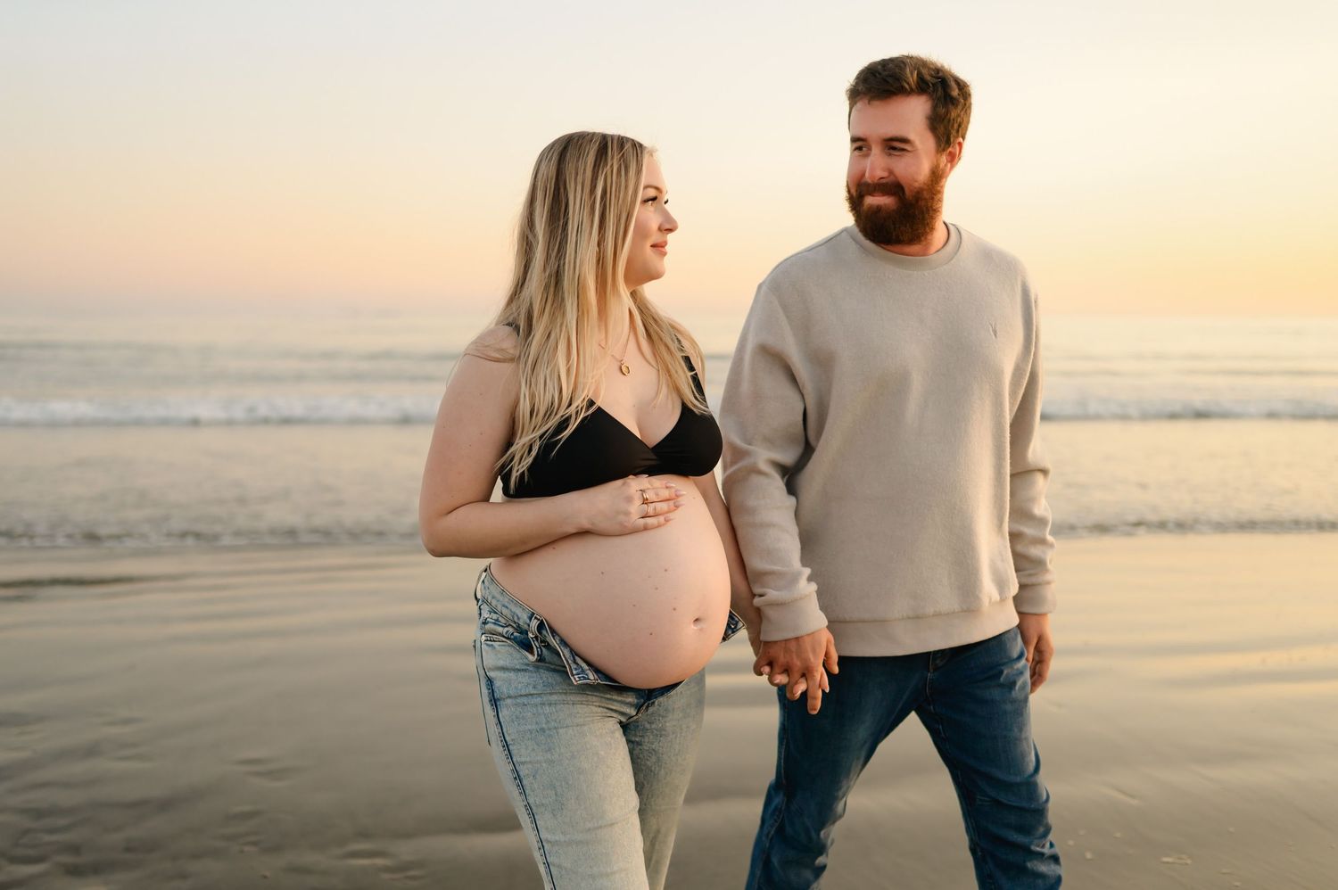 Santa Barbara babymoon maternity photoshoot by Ventura maternity photographer of mama in jeans and sports bra walking on Carpinteria beach