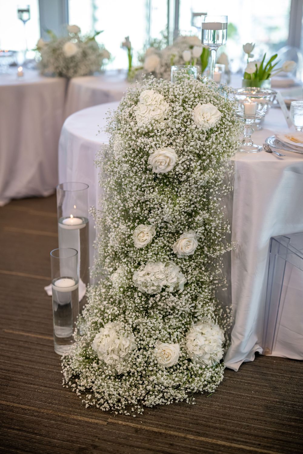 Elegant baby's breath and white rose floral cascade arrangement with glowing candles at a wedding reception.