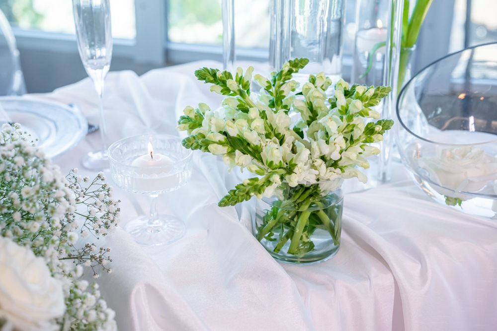 White floral centerpiece with delicate blooms in glass vase on light tablecloth.