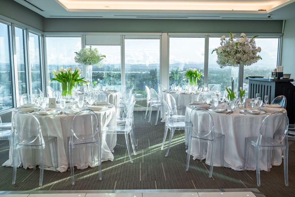 Modern reception venue with round tables and city views through floor-to-ceiling windows.