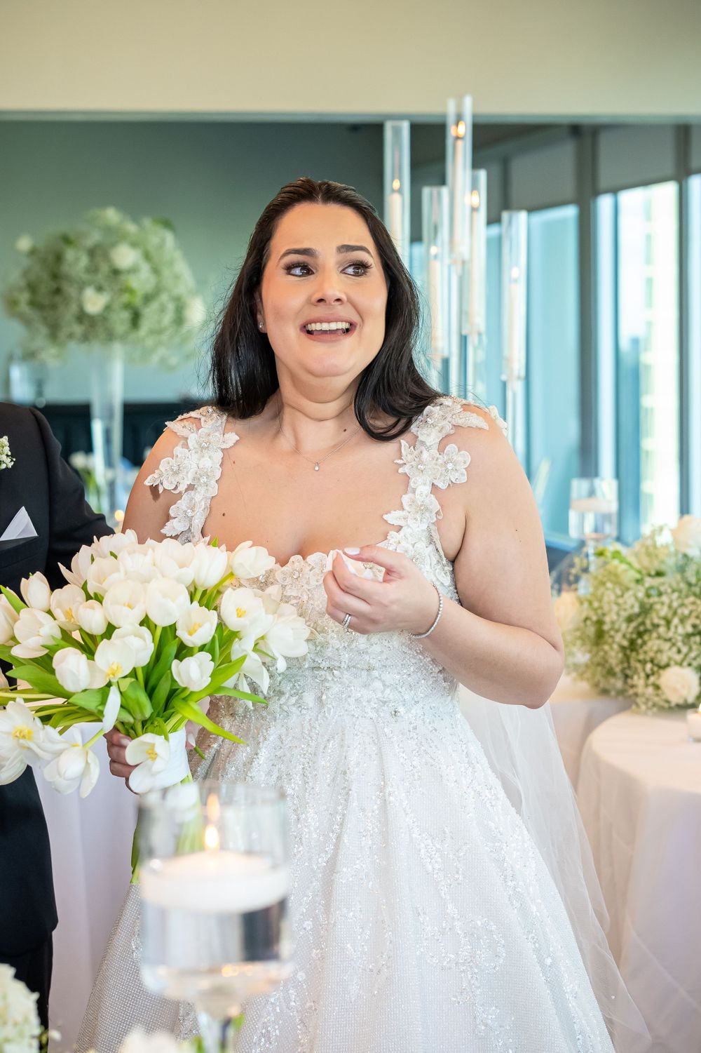 Bride in lace gown expressing joy during wedding reception.