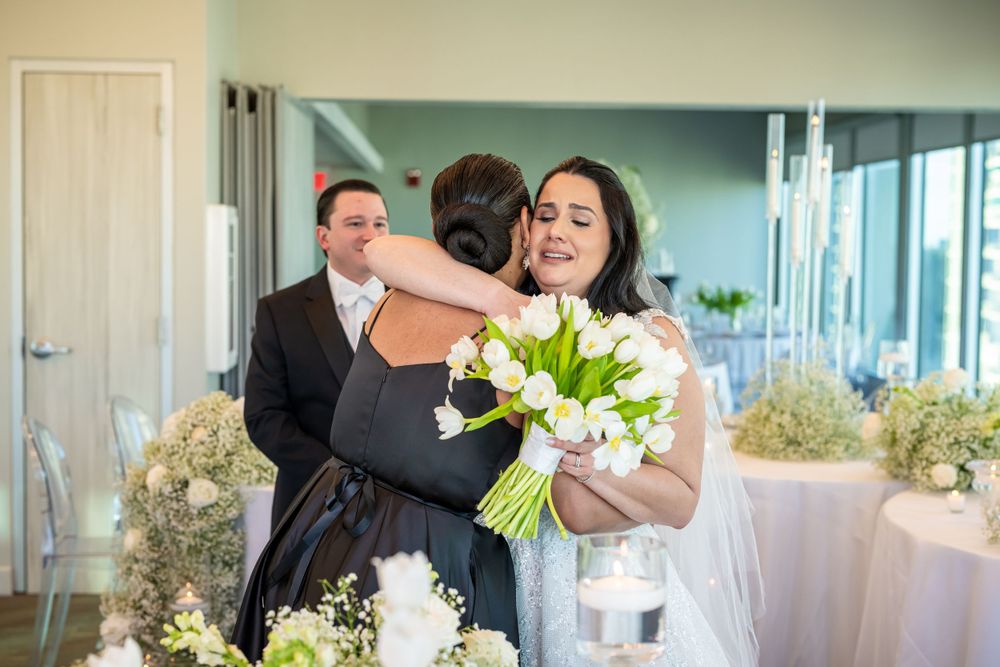 Wedding celebration with white floral arrangements and emotional embrace in elegant venue.