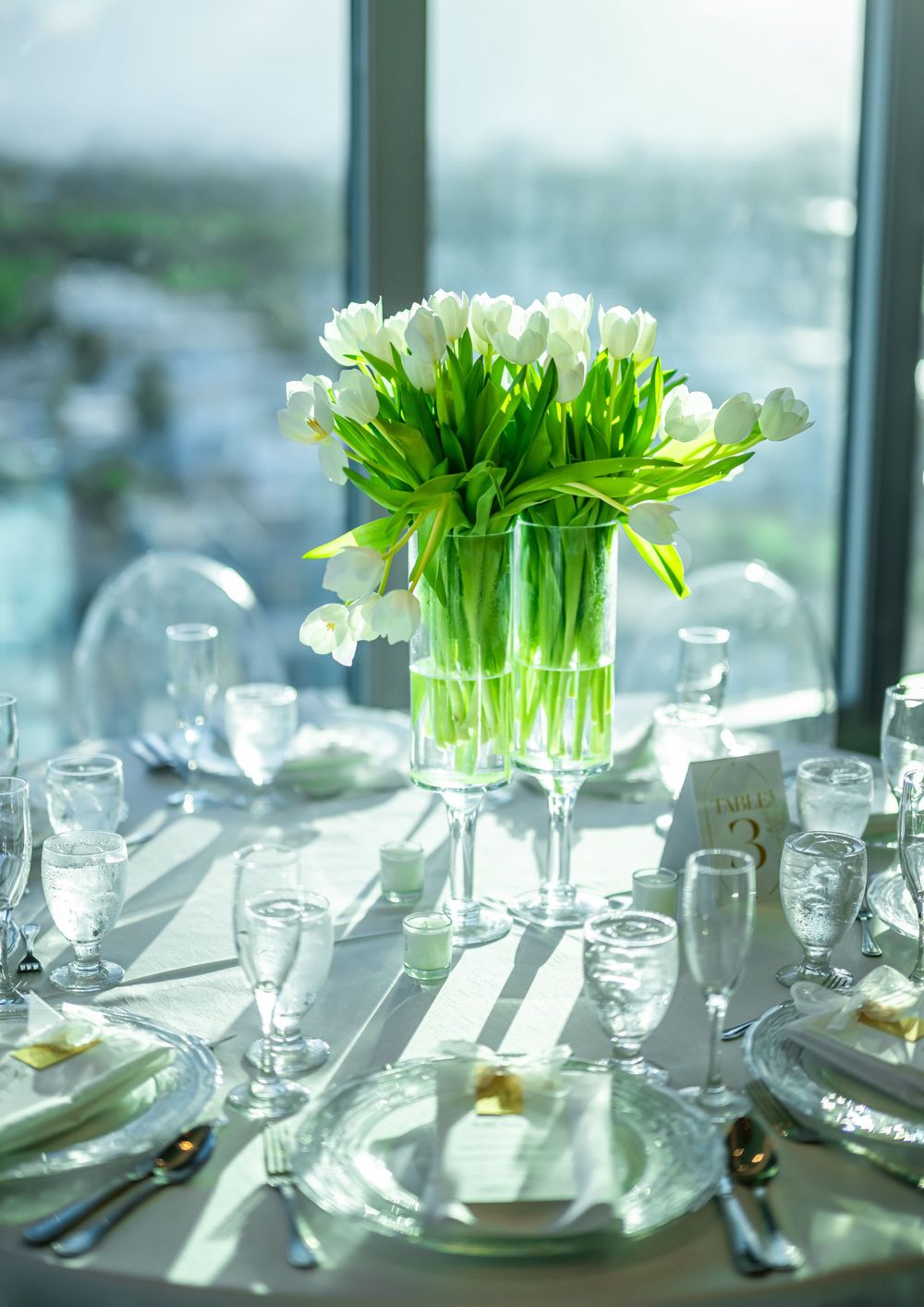Fresh white tulips in crystal vase centerpiece with formal table settings.