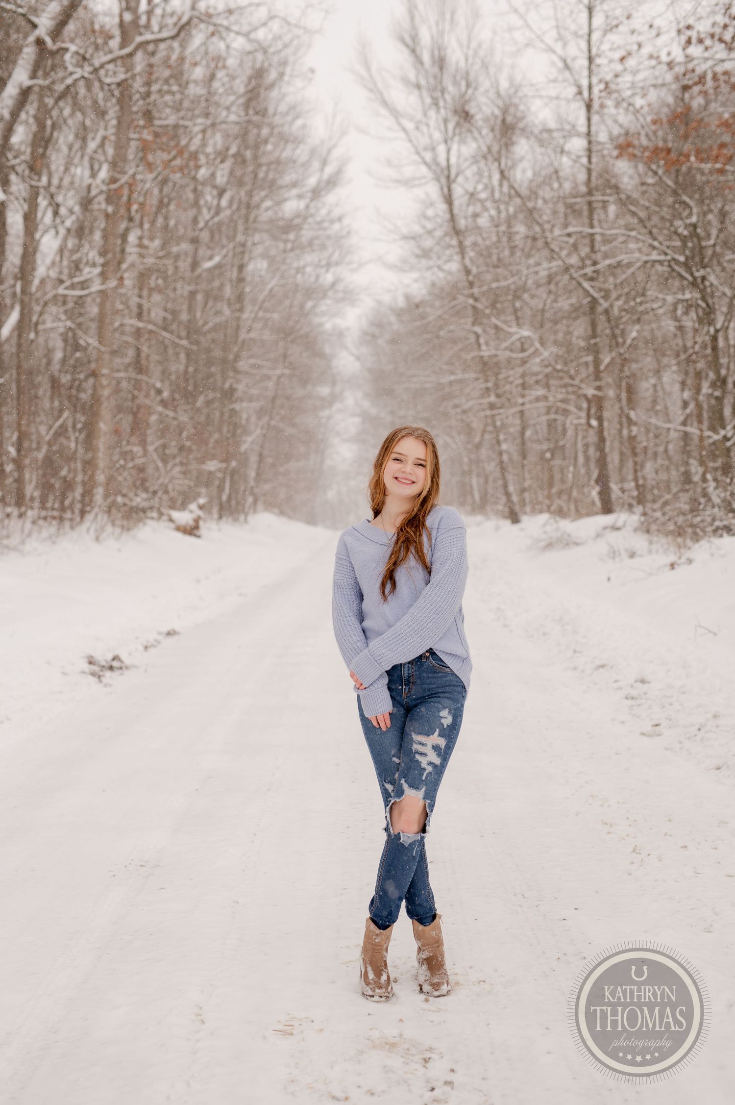 A person in casual winter attire poses on a snow-covered forest trail.