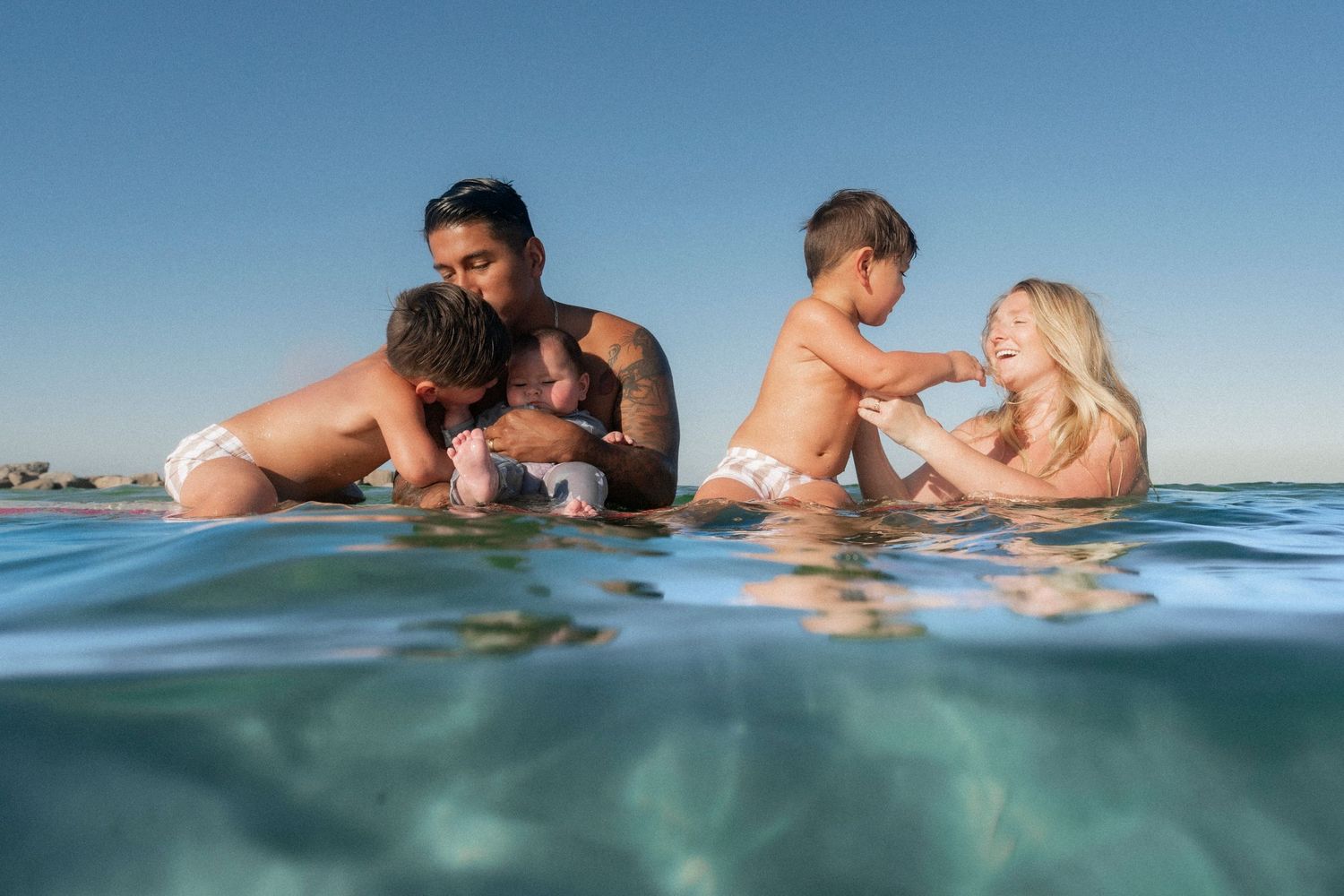 A joyful family enjoying an underwater photoshoot at the Destin Jetties, surrounded by clear emerald water and bright skies.