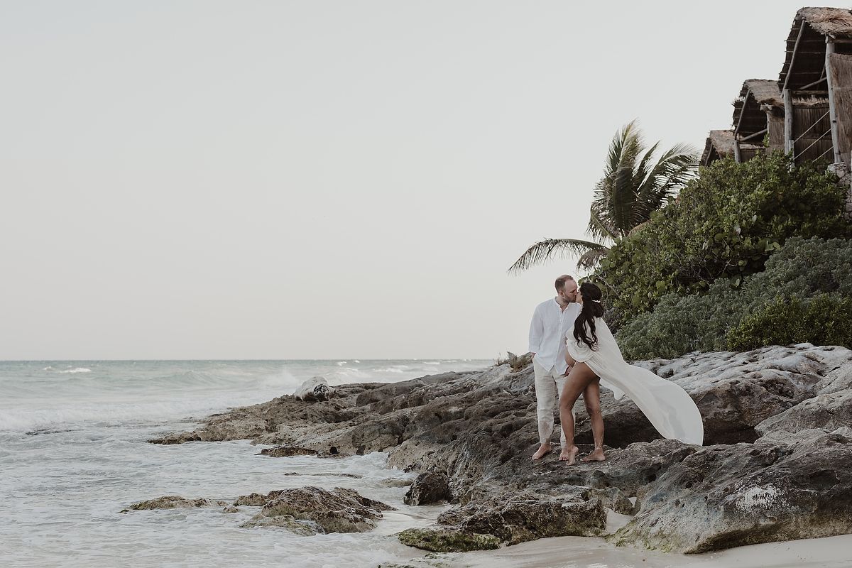Couple kissing on rocky shoreline with ocean backdrop during a romantic beach photoshoot in  our Habitas Tulum.
