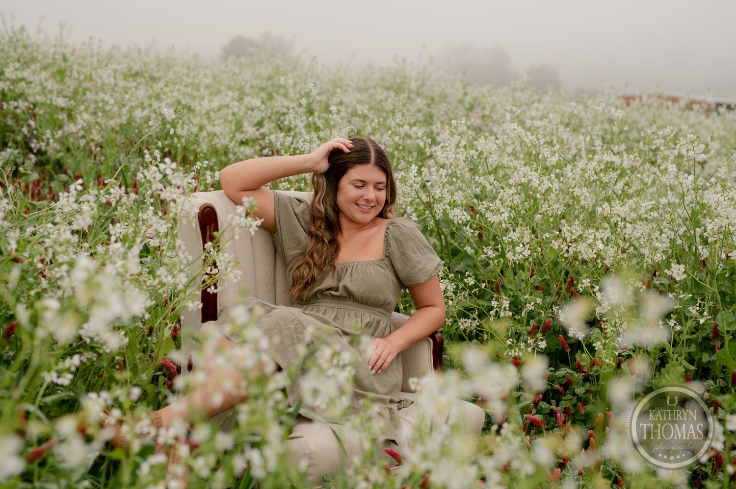 A woman relaxes in a vintage chair amidst a field of white wildflowers at dusk.