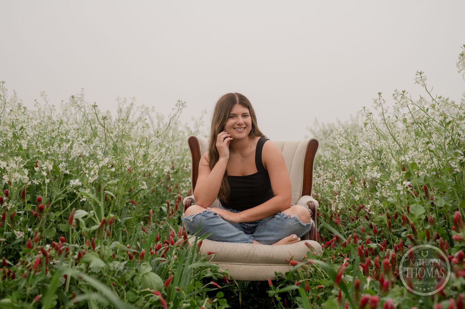 Casual outdoor portrait session featuring a beige armchair placed in a meadow of white and red flowers.