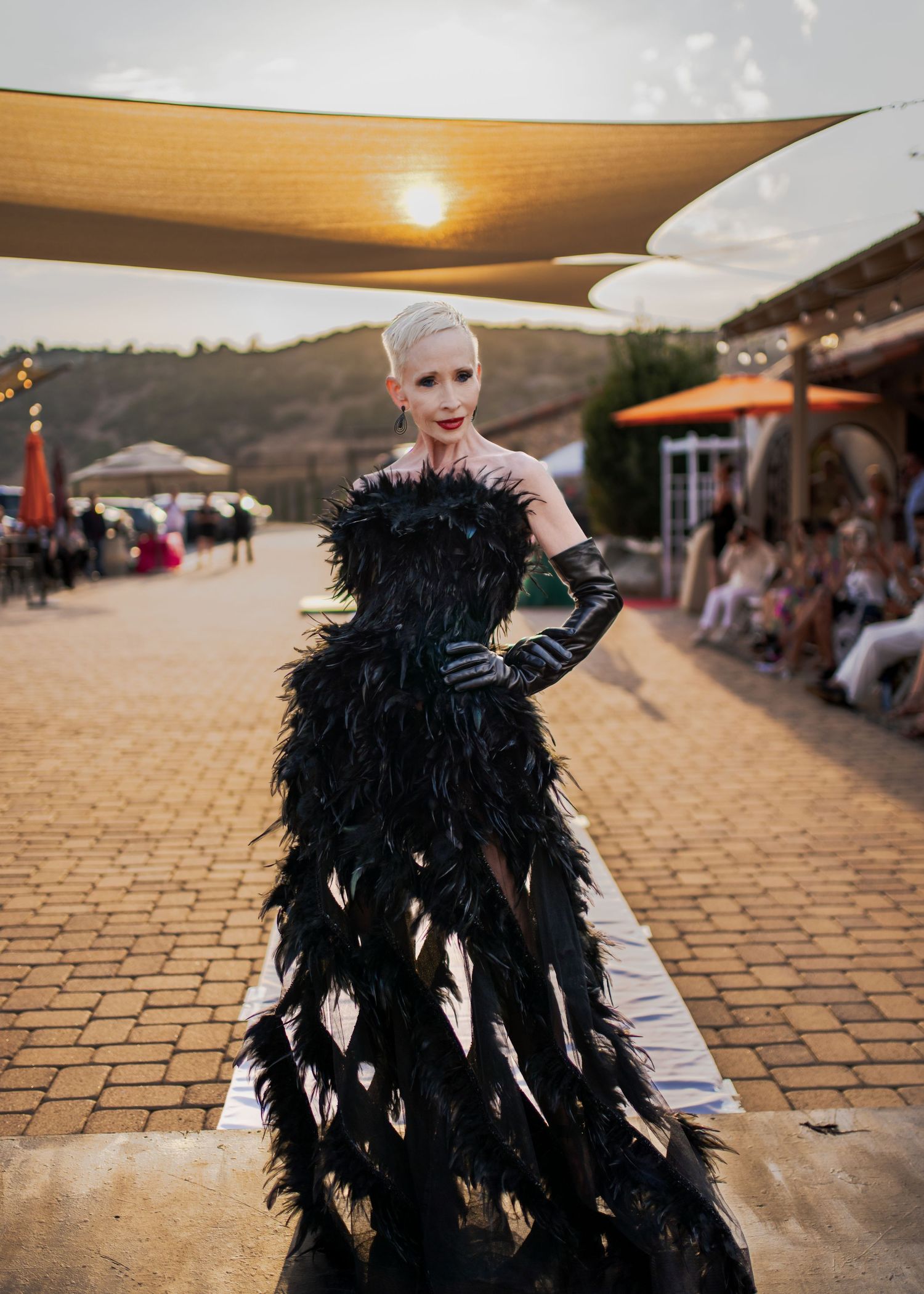 Dramatic black feathered evening gown with corset bodice displayed at outdoor sunset fashion show.