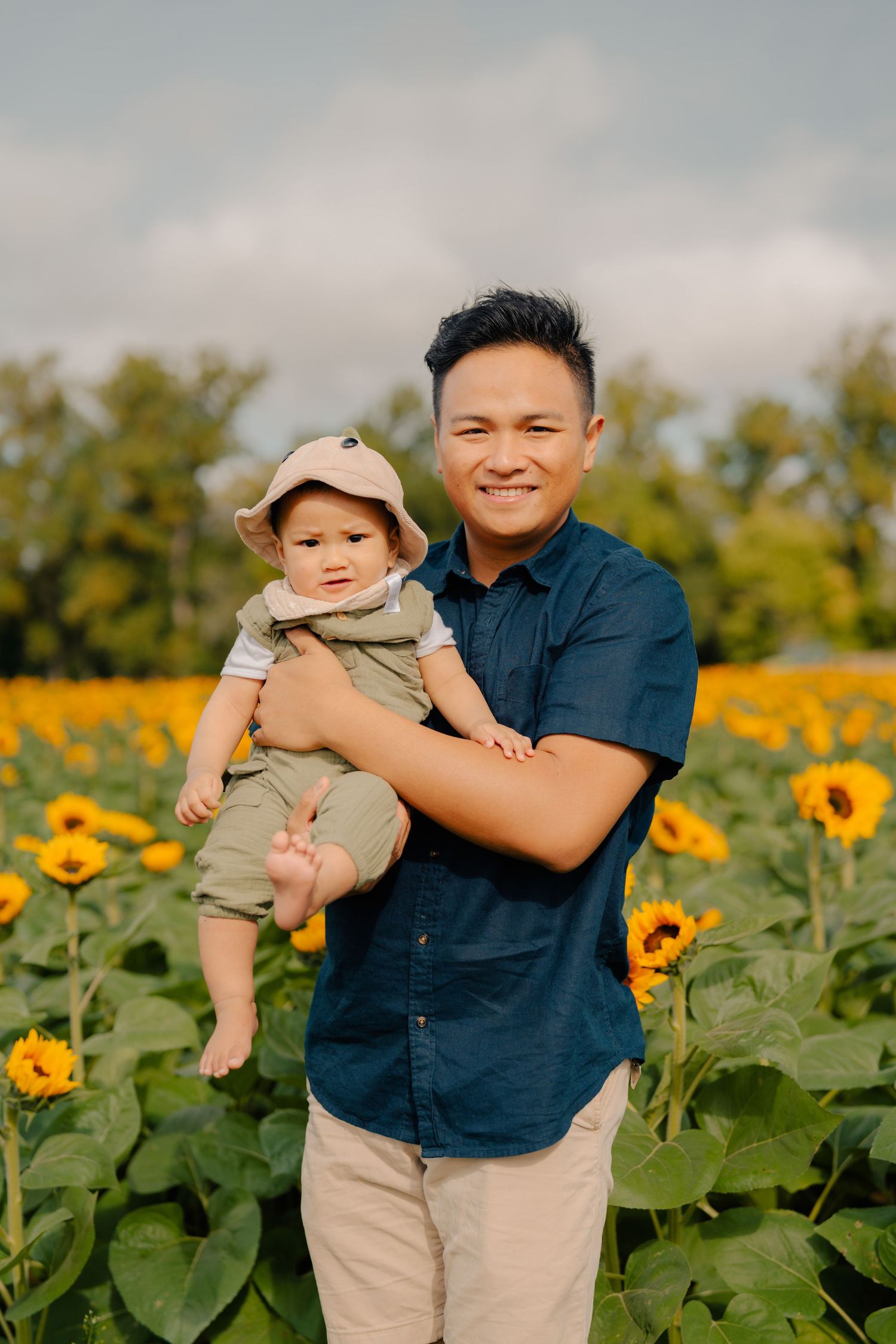 A tender moment in a sunflower field showing a parent holding a baby among bright yellow blooms.