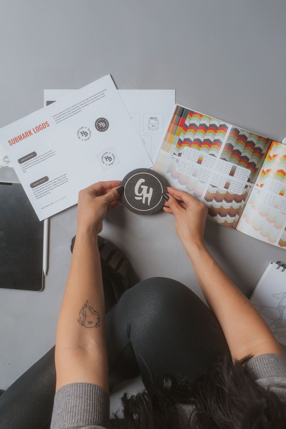 Overhead view of hands holding a branded logo coaster with marketing documents spread on desk.