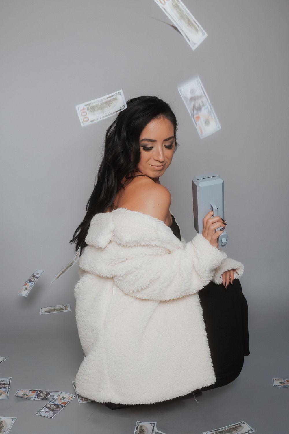 Money falling around a woman in a cozy white sweater during a creative photoshoot.