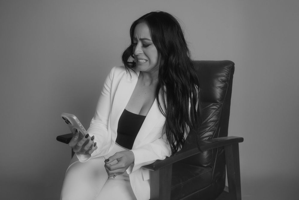 Professional wearing a white blazer smiles while looking at phone in black and white portrait.