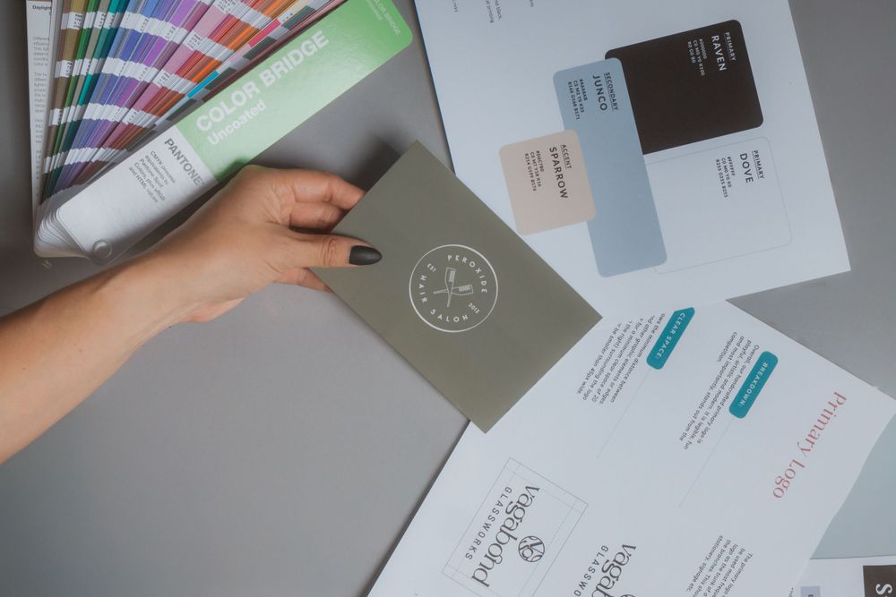 Hand holding color swatches over business documents and branding materials.