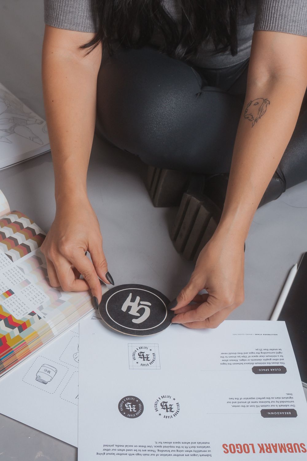 Hands working on business documents with logos and branding materials on a white desktop.