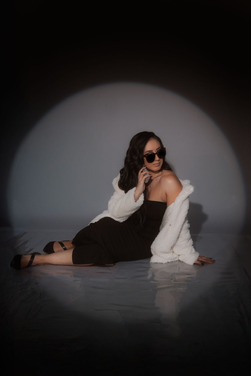 Dramatic studio portrait in spotlight featuring person in black dress and white fur coat.
