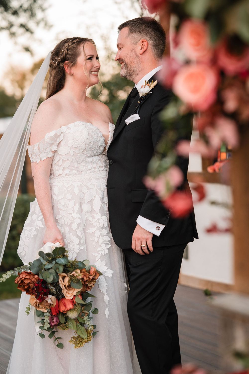 Wedding couple sharing romantic moment on wooden deck with autumn floral decorations.