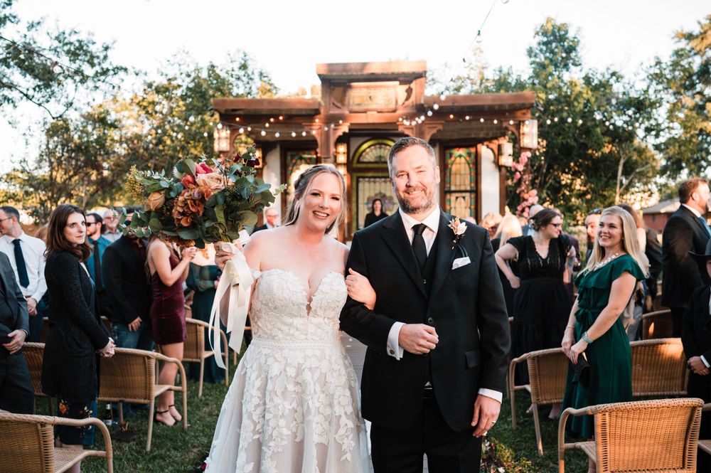 Outdoor wedding celebration with guests gathered on a patio with rattan furniture.