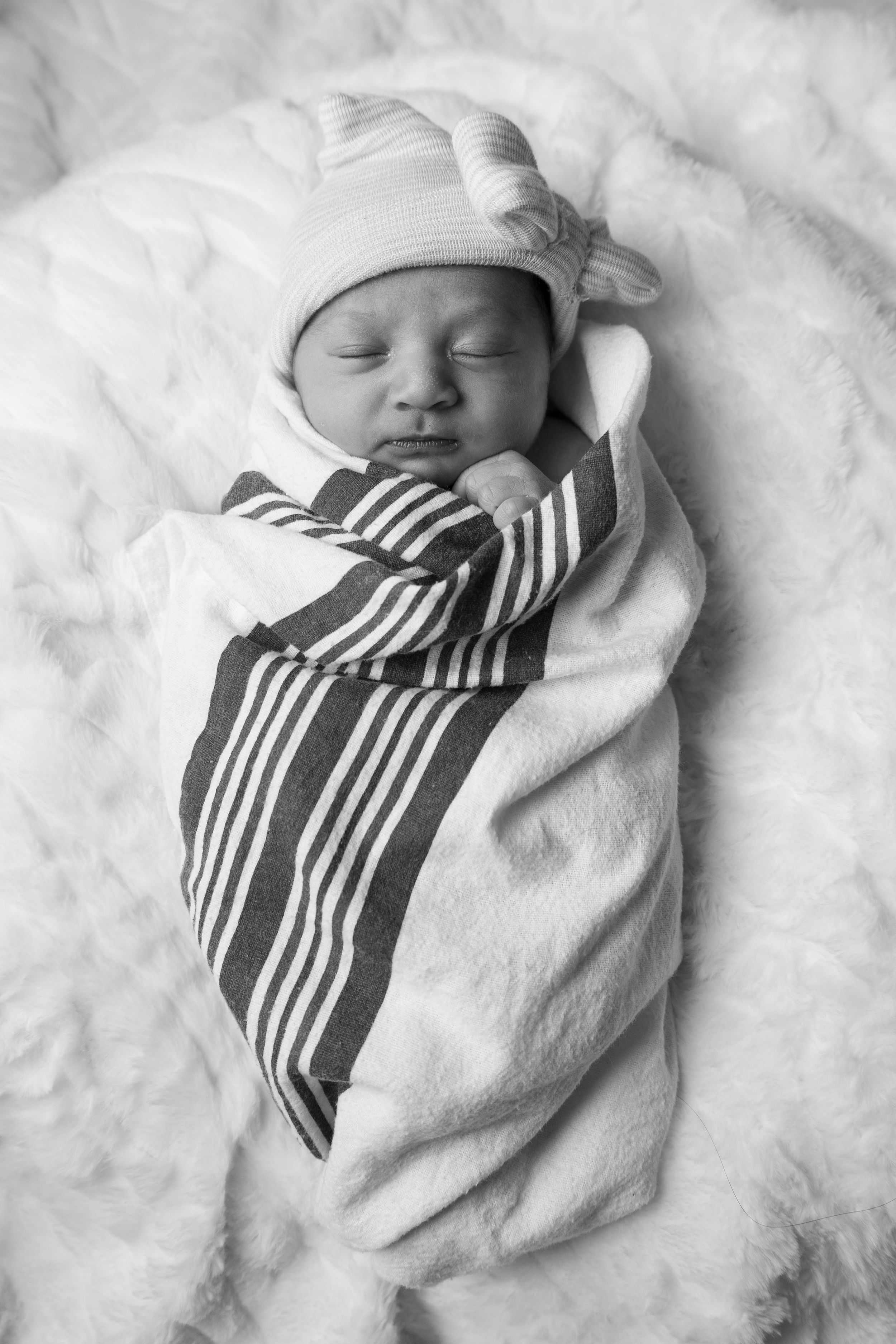 Sleeping newborn wrapped in striped blanket and white hat resting on soft white bedding.