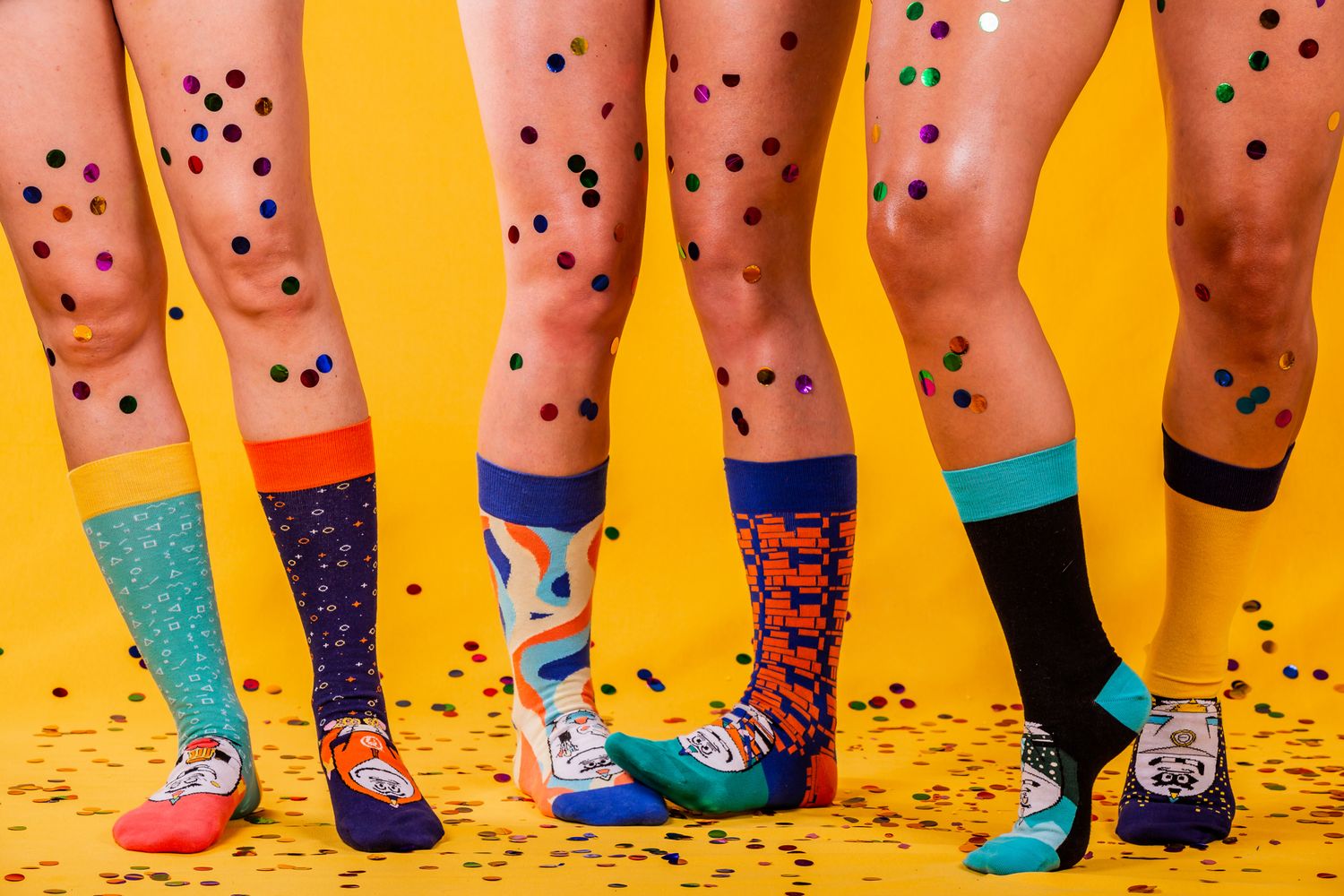 Colorful mismatched socks and confetti against yellow background in fun fashion composition.