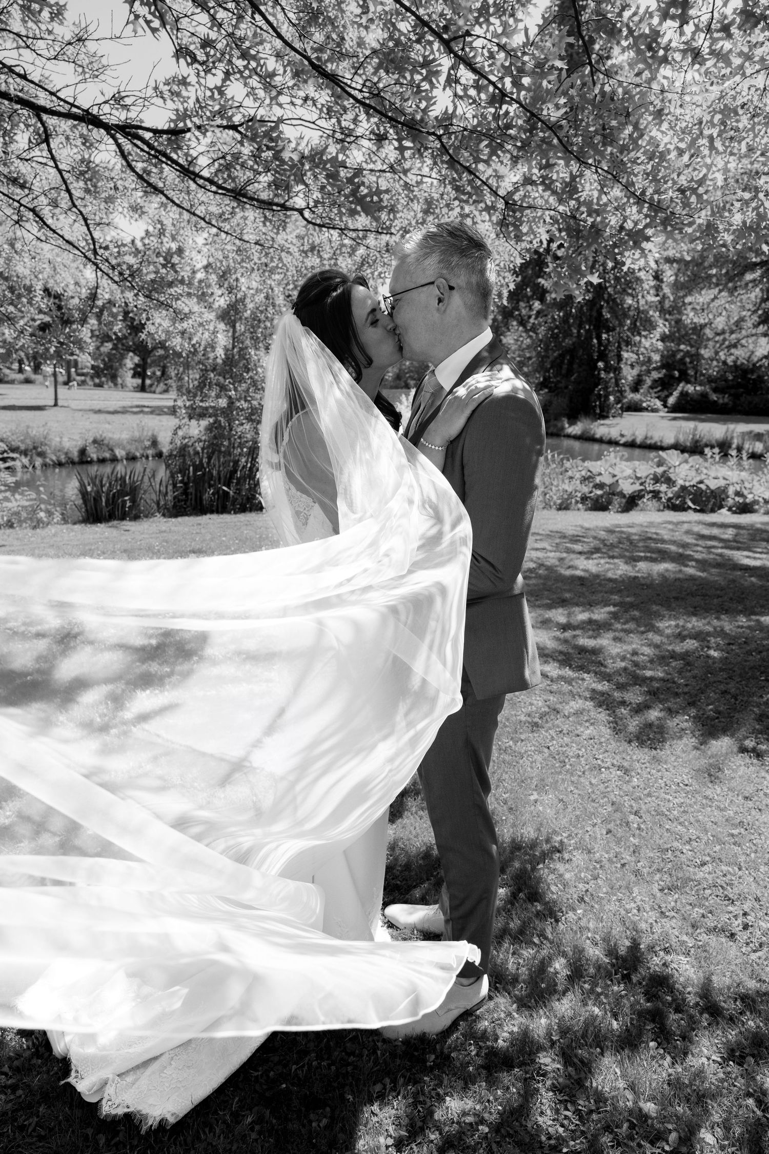 A romantic black and white wedding photo captured outdoors with flowing white dress veil billowing in the breeze.