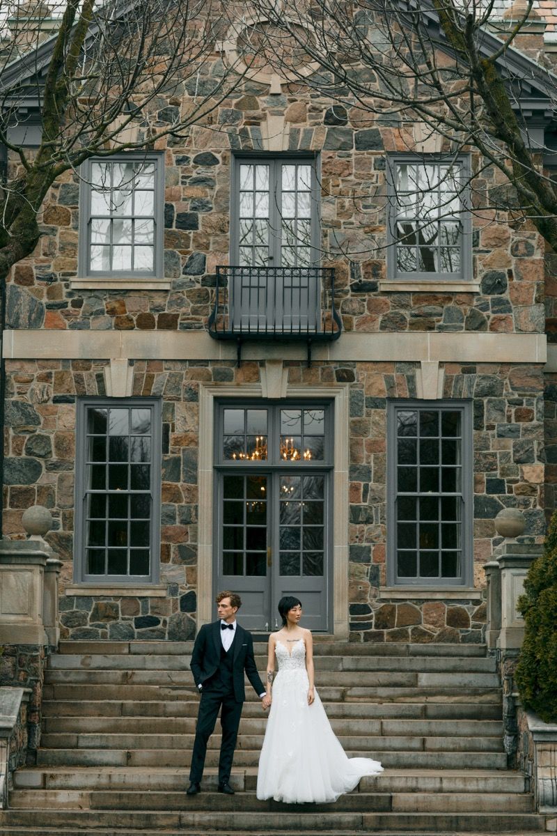 A formal wedding portrait in front of a stone building with elegant windows and architecture.