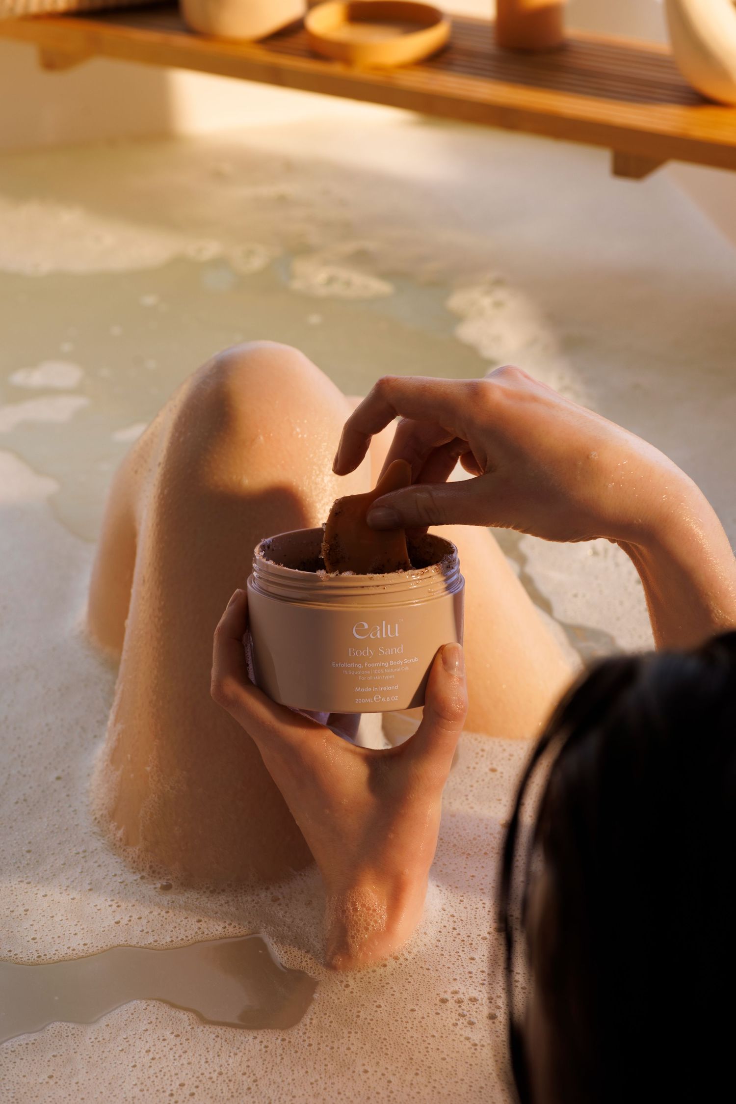 Hands holding skincare product jar in luxurious bubble bath setting.