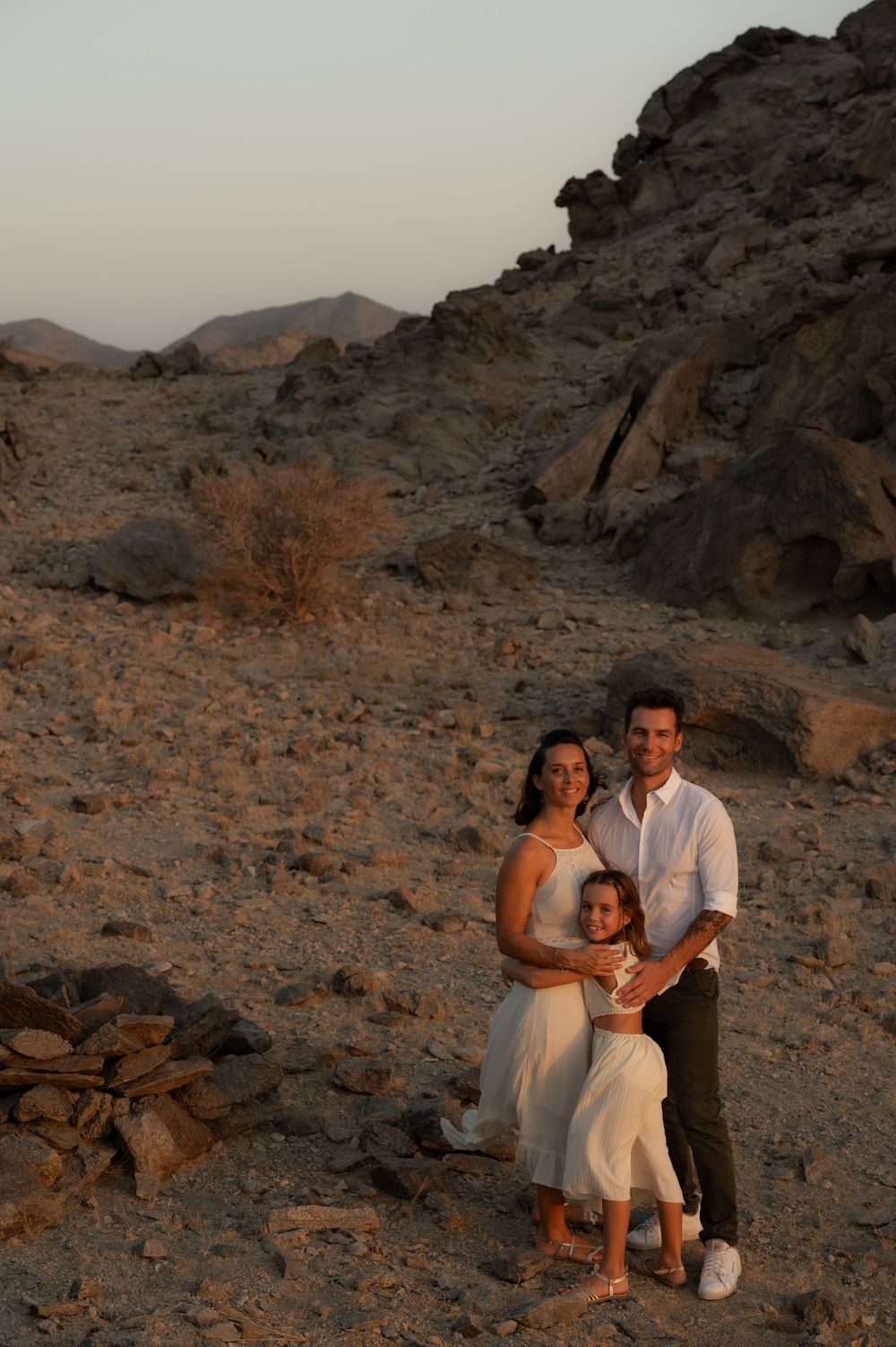 Family enjoying moment together on rocky desert terrain at dusk.