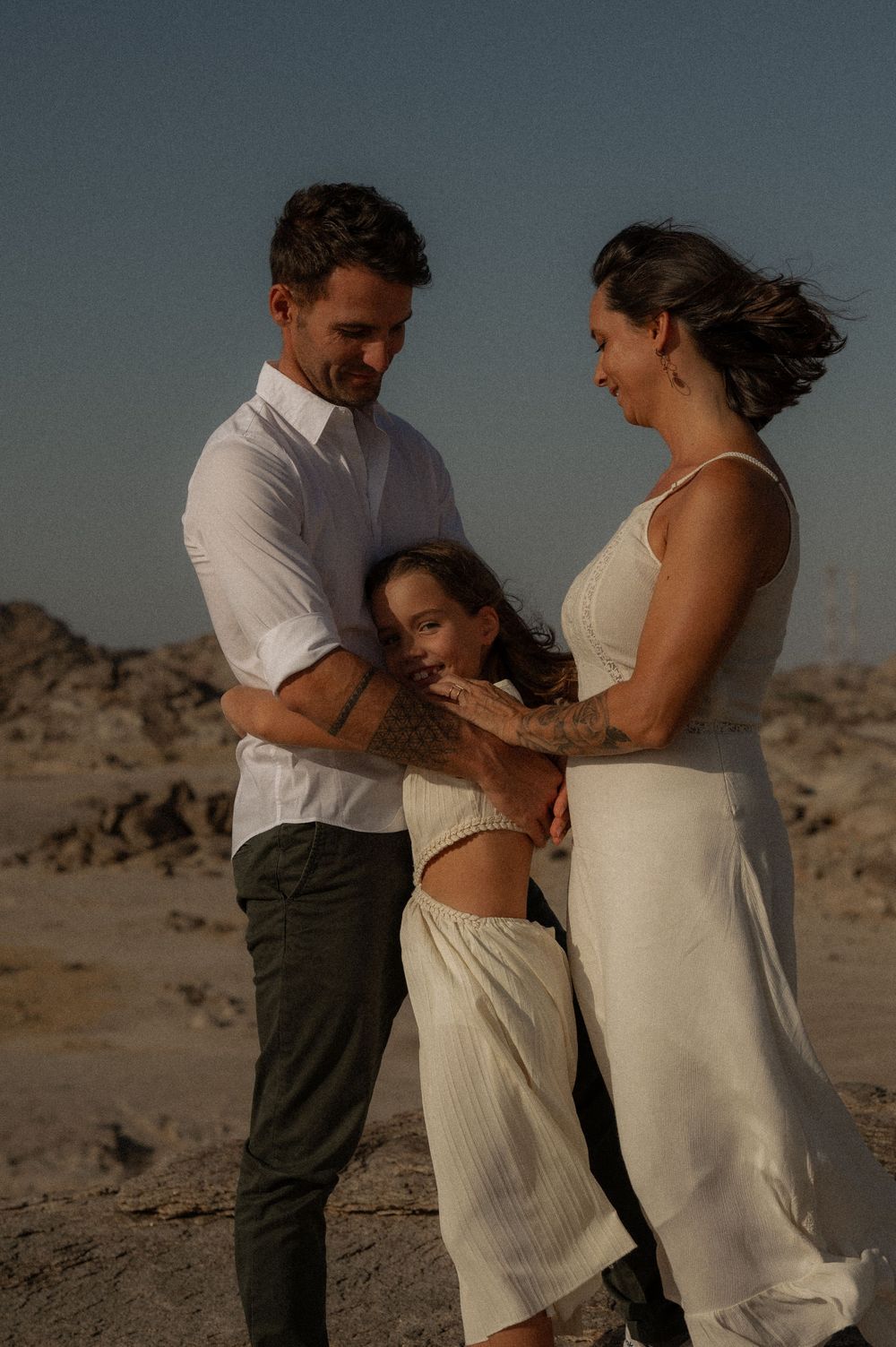 Family embracing in white clothing against desert backdrop during sunset.