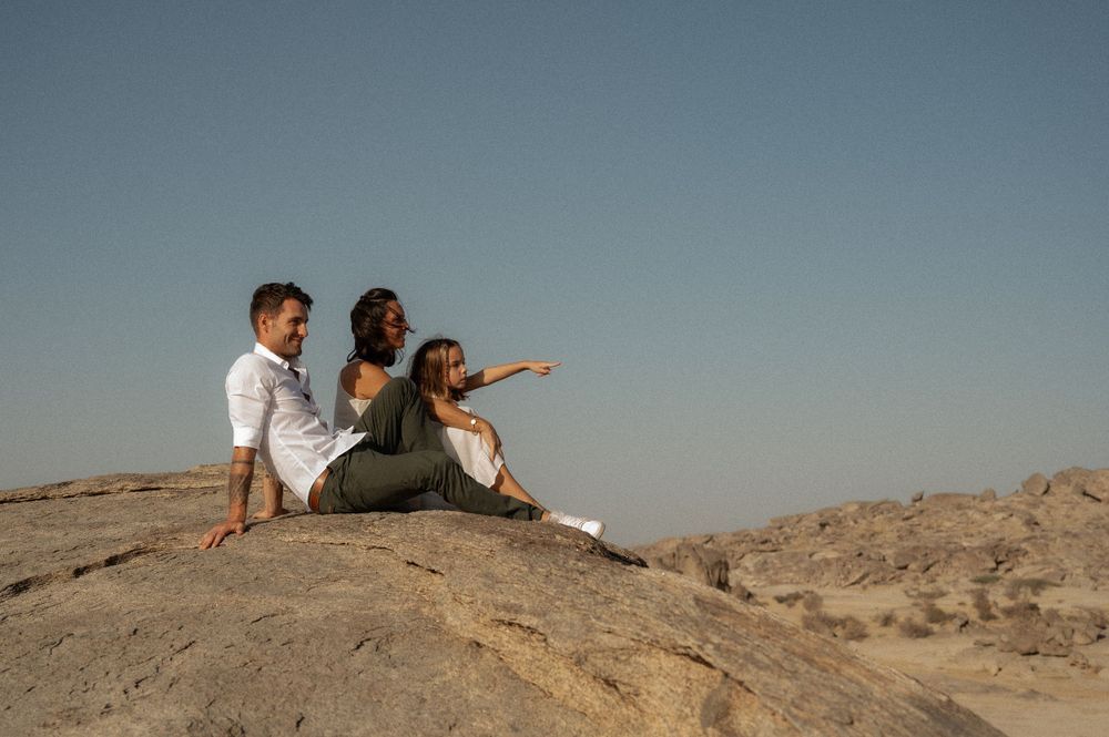 People sitting on desert rocks overlooking vast landscape at sunset.
