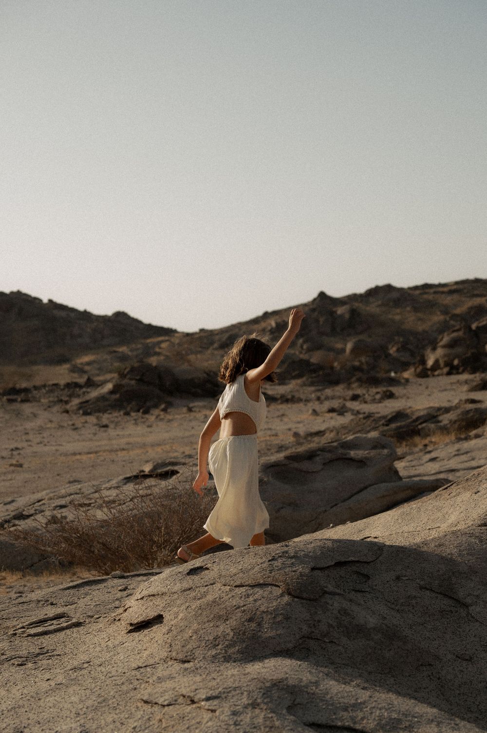 People in white clothing exploring rocky desert terrain during golden hour.