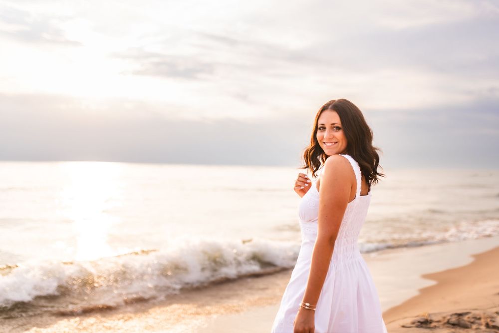 Senior portrait of a girl looking back at the camera on the beach with the waves crashing behind her.