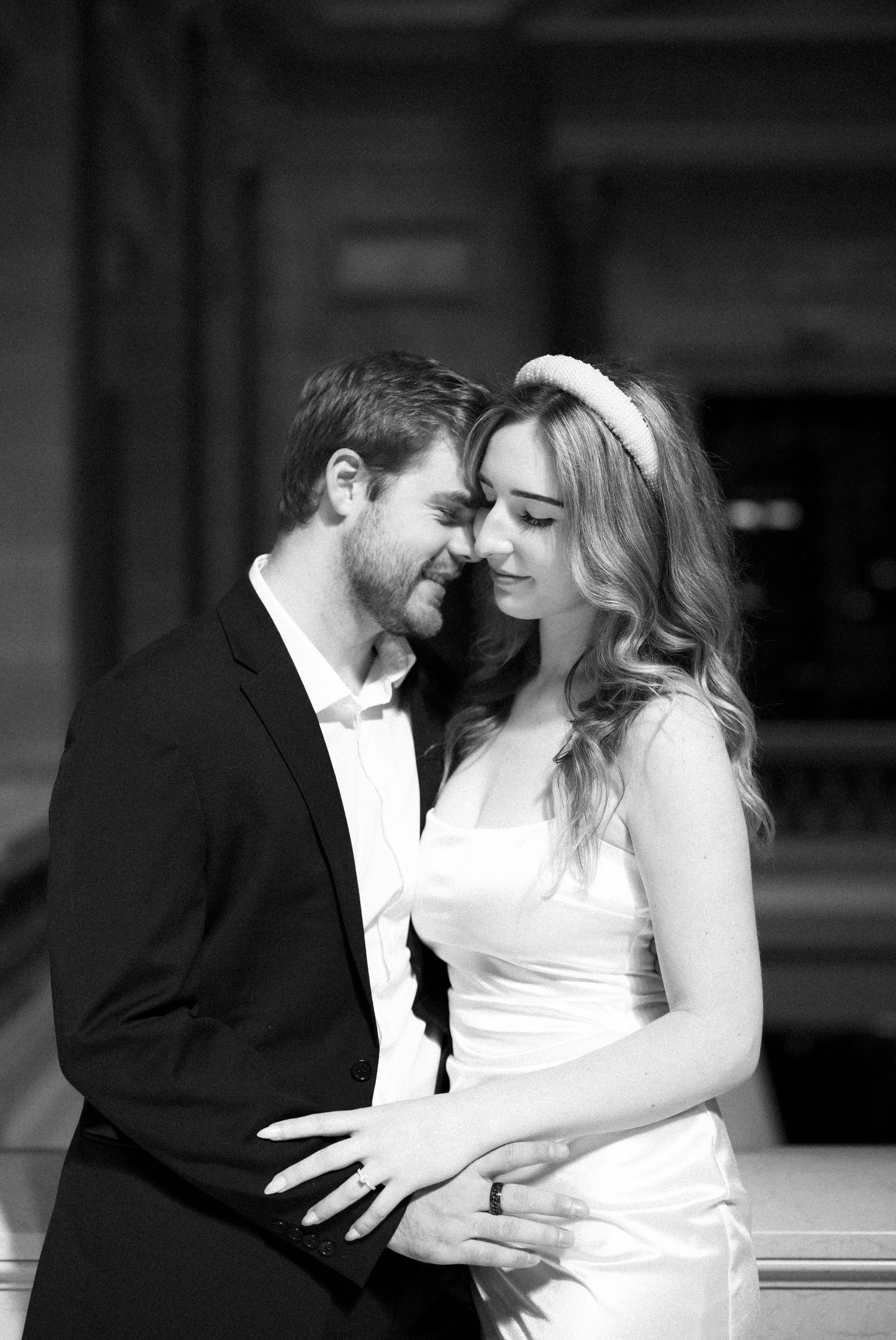 Black and white wedding photo of a couple in formal attire sharing an intimate moment with their eyes closed.