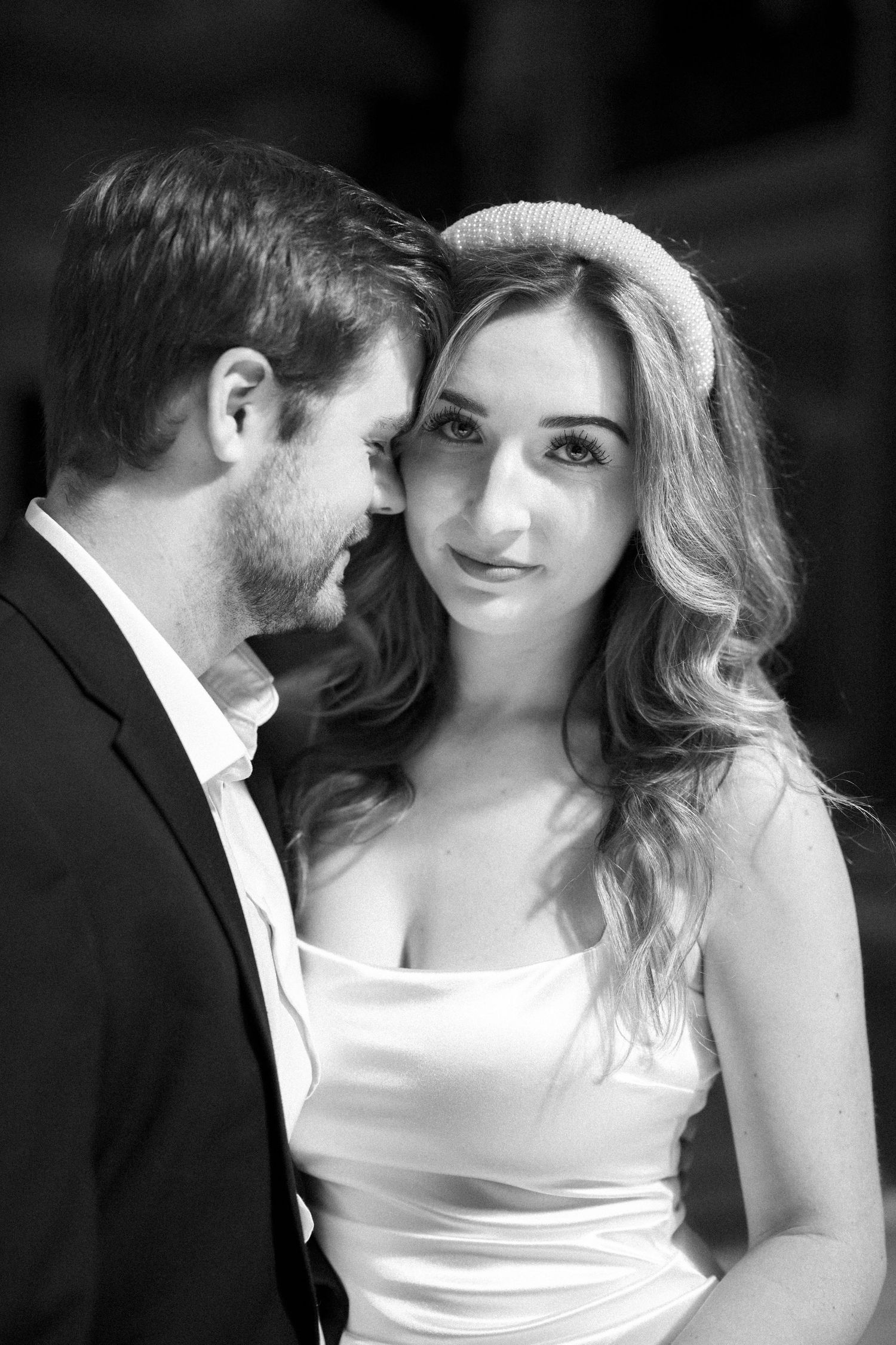 Black and white portrait of a bride in a white dress and groom in a dark suit in an intimate romantic moment.