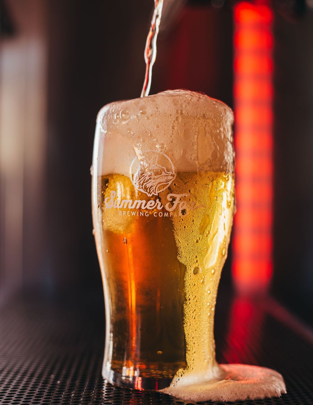 Beer pouring into and overflowing from a Summer Fox beer glass
