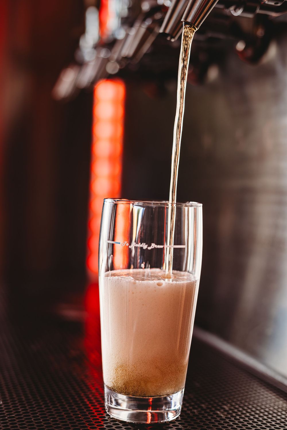 Beer pouring into a Summer Fox Brewing pint glass under red bar lighting