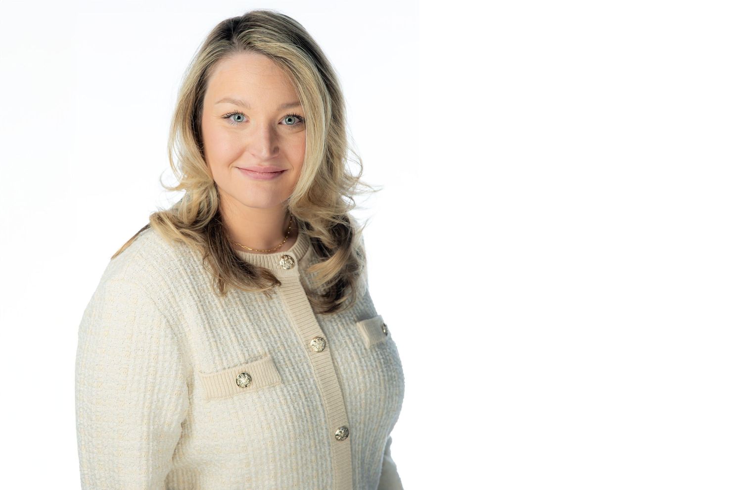 A person wearing a cream colored sweater smiles warmly against a white background in a professional headshot.