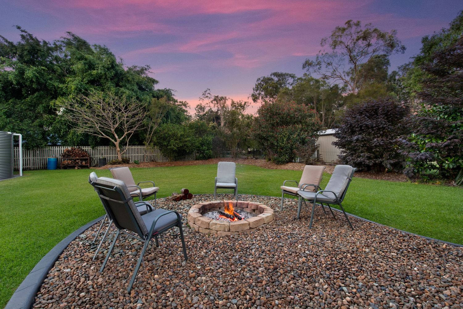 Cozy outdoor fire pit seating area surrounded by lush garden at dusk.