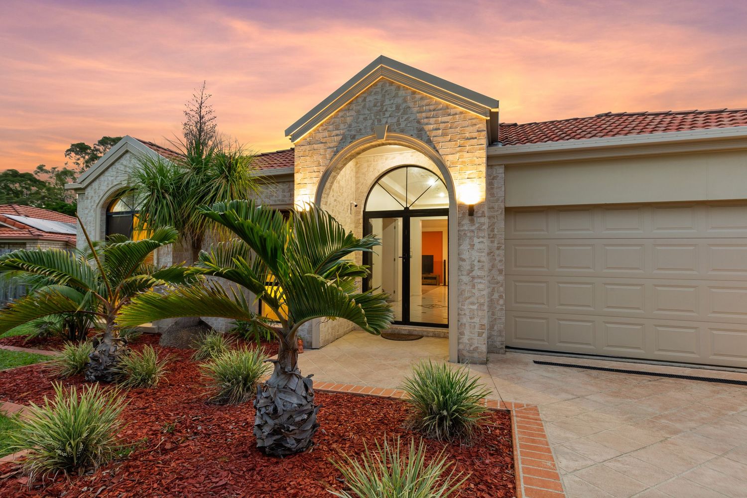 Grand arched entrance with decorative stonework and tropical garden landscaping at twilight.