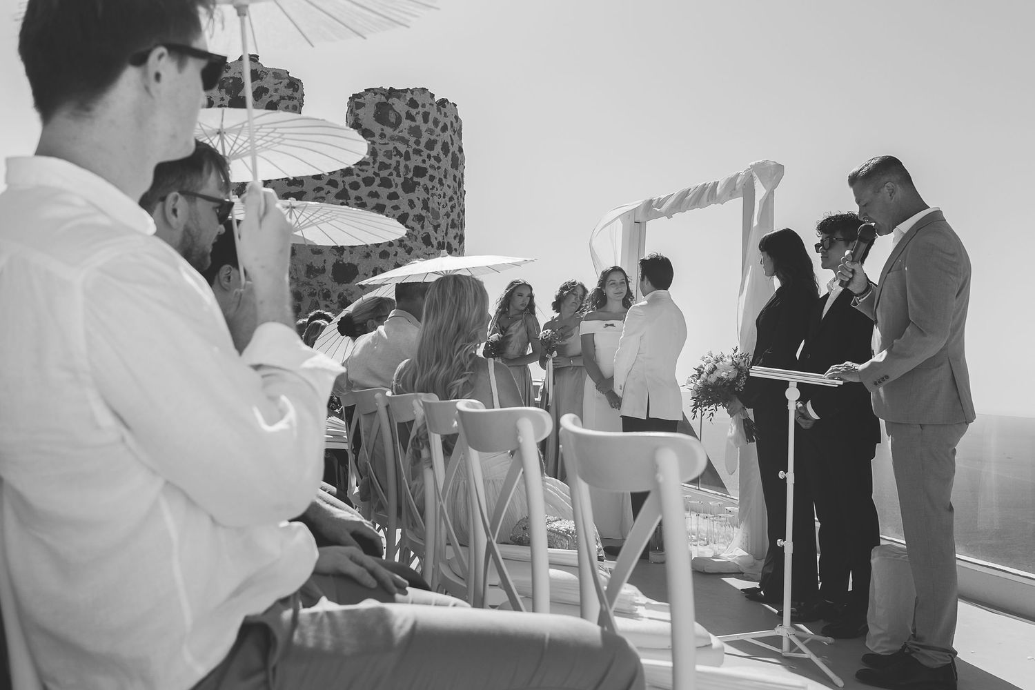 Black and white photo of people gathered outdoors on a terrace with guests holding parasols.
