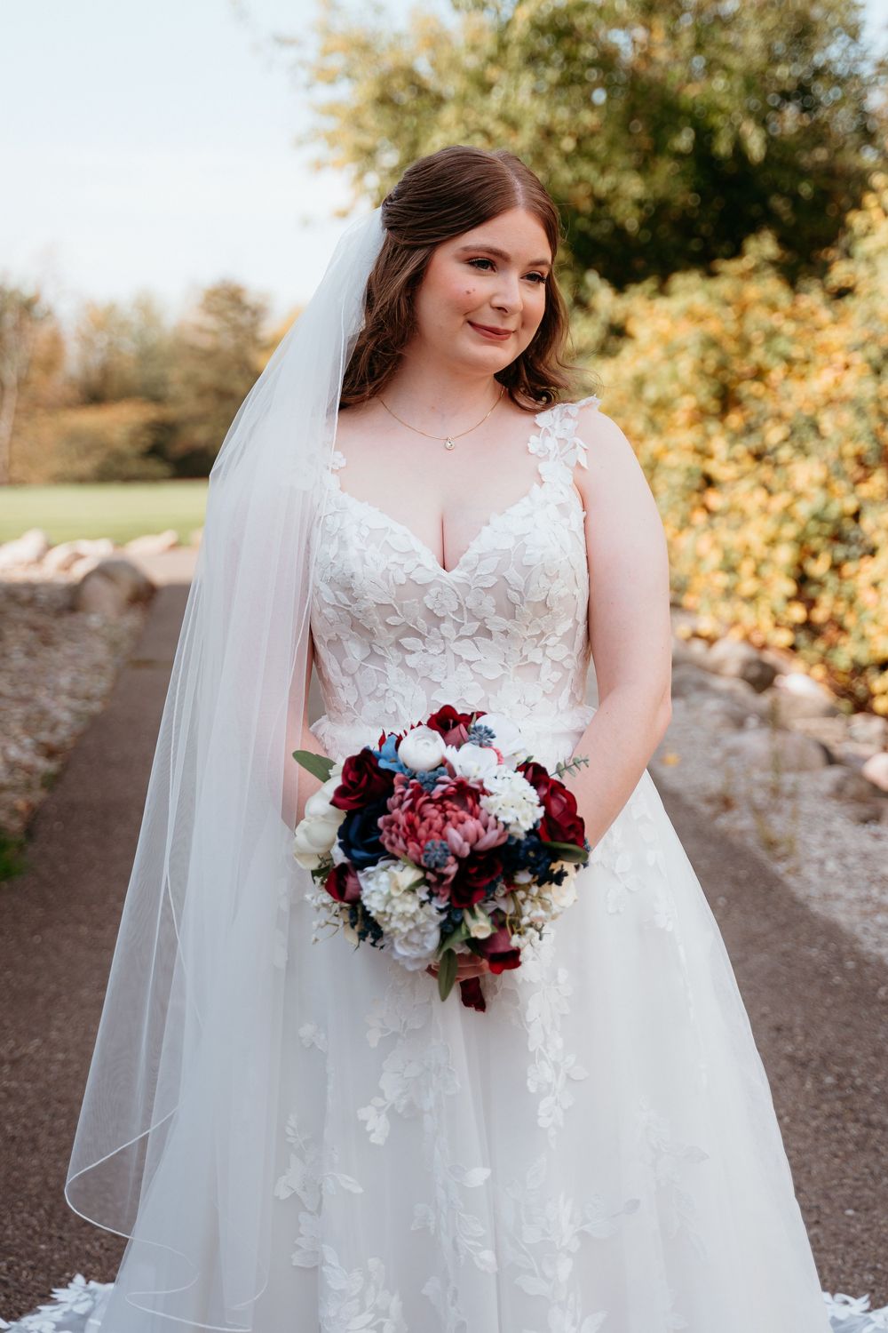 White wedding gown with lace details and burgundy bouquet photographed outdoors in autumn.