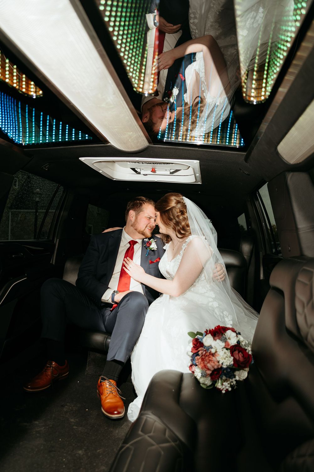 Newlyweds share an intimate moment in the back of a limousine with decorative lighting.