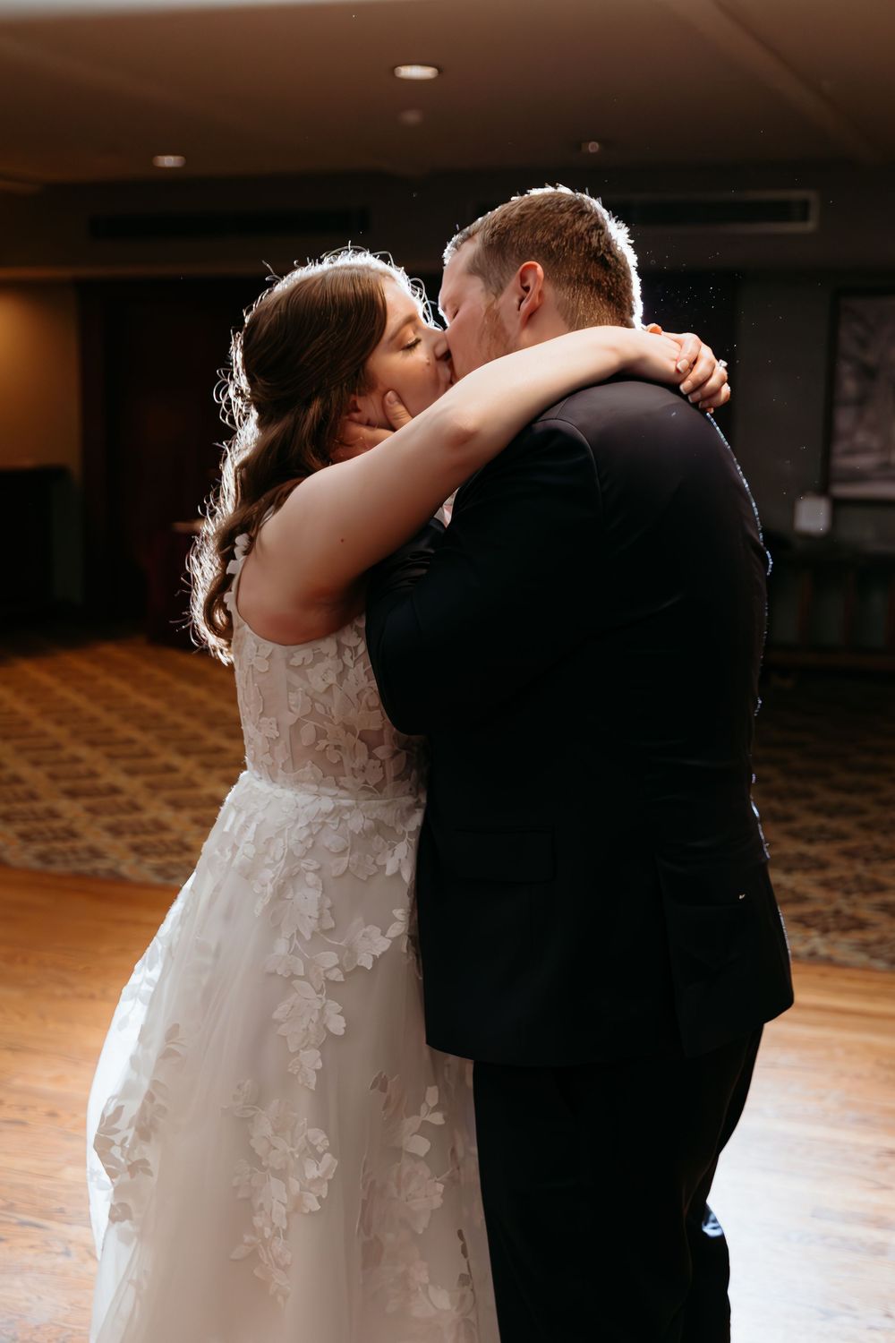 A romantic first dance moment captured in warm lighting on a wooden dance floor.