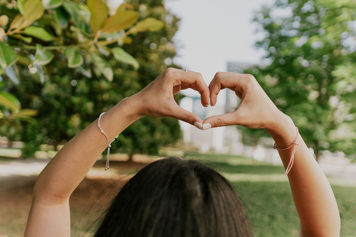Hands forming a heart shape against a green natural background during graduation.