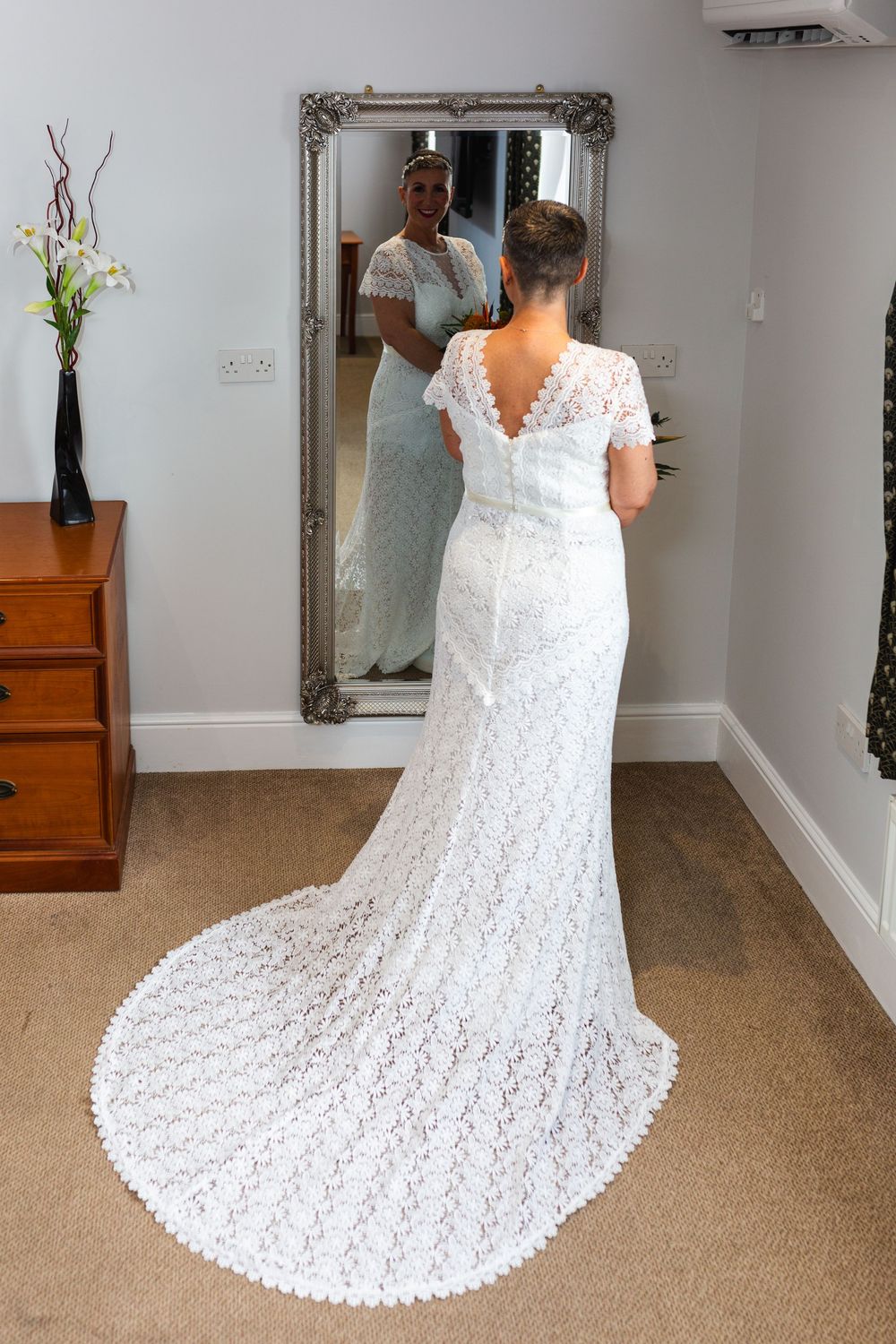 A stunning white lace wedding dress with an elegant cathedral-length train displayed in a room with hardwood floors and mirrors.